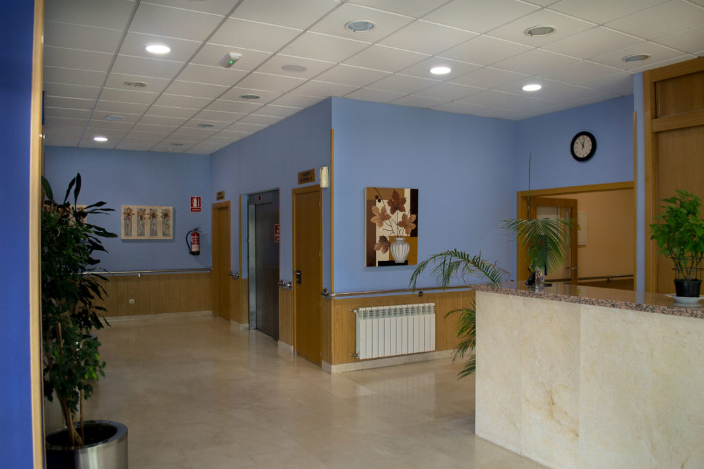 Recepción en la Residencia Cuidad de Aranda, con suelos amarmolados, ascensor y decoración con cuadros y plantas naturales.